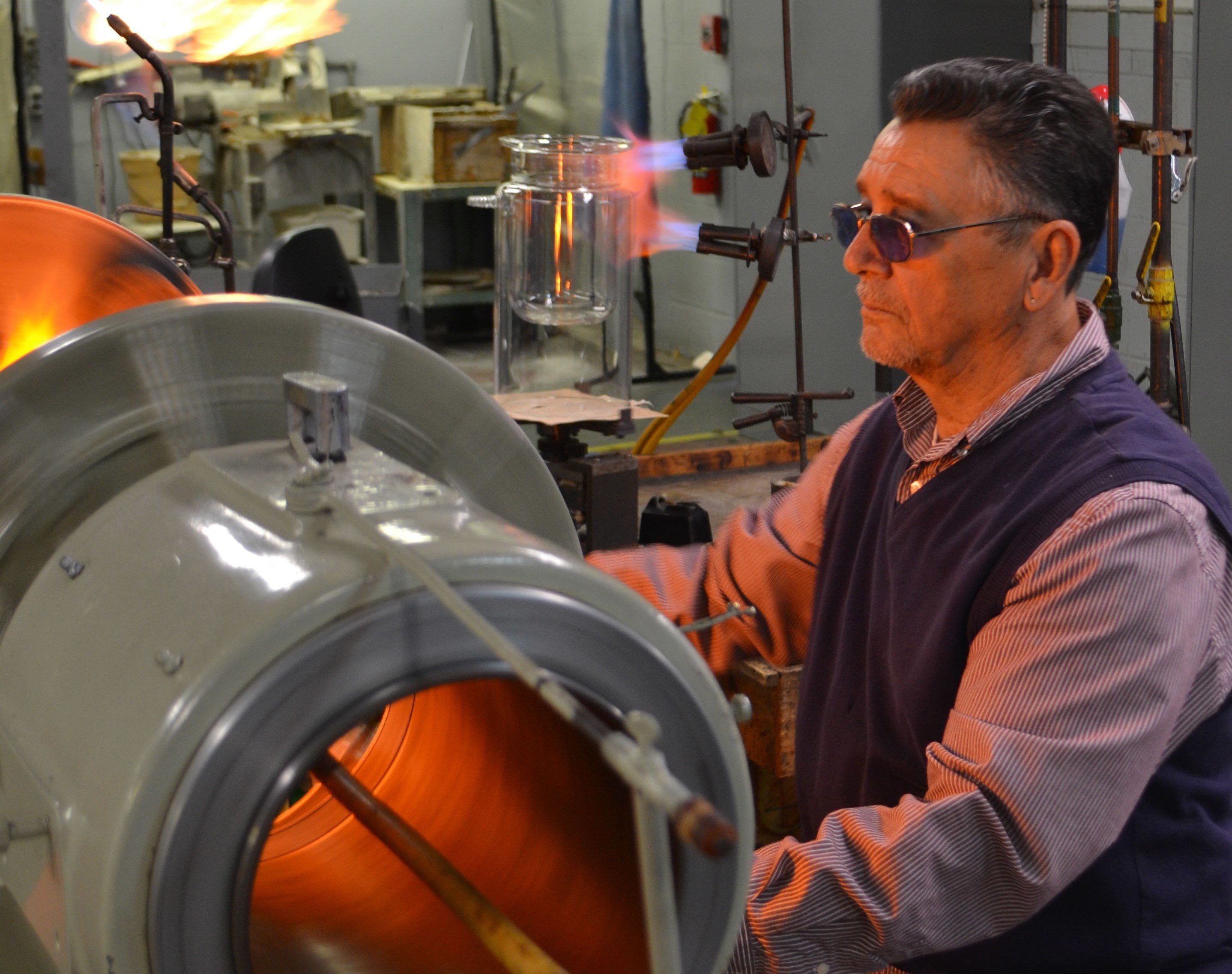 A man with goggles on blowing glass.
