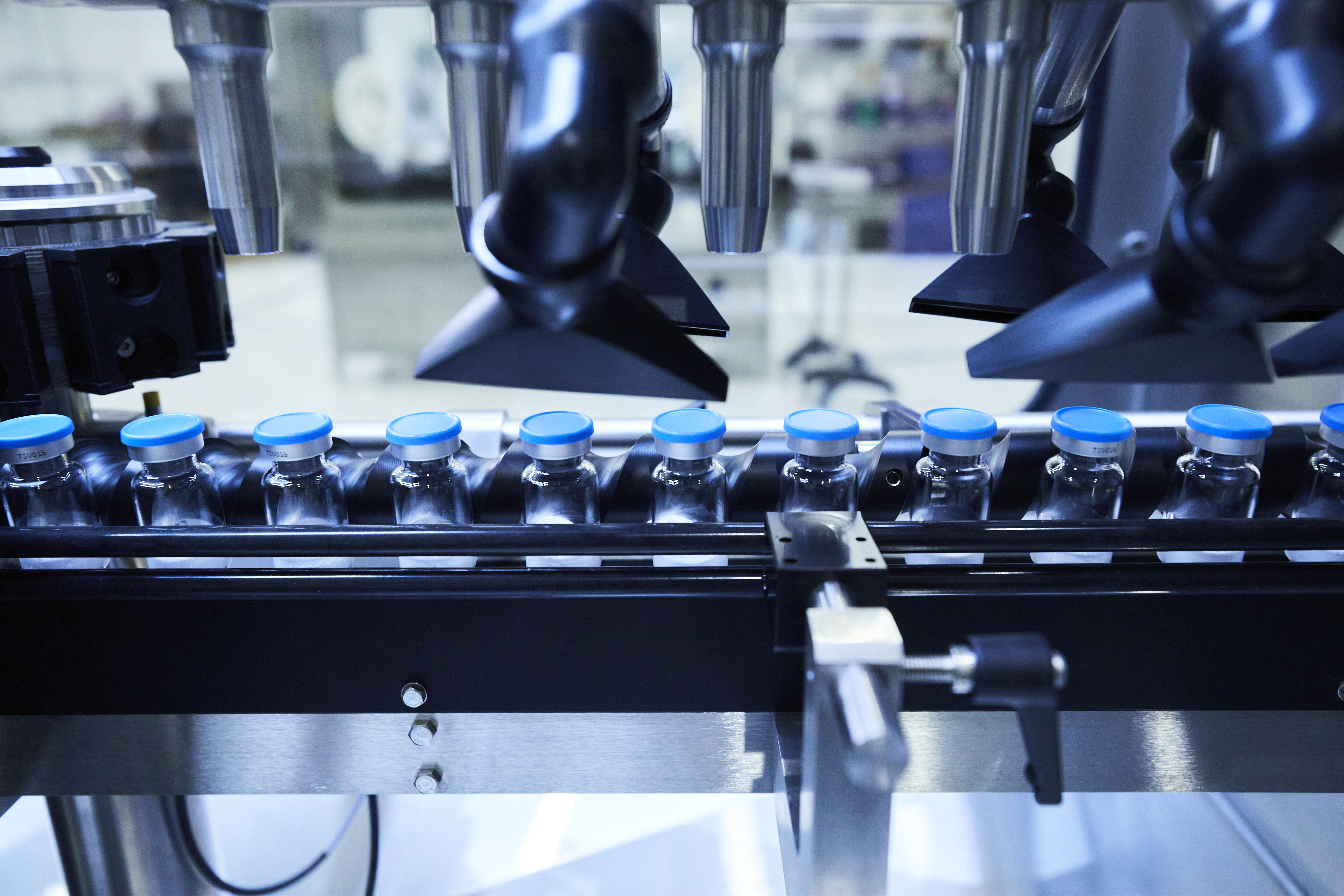 Conveyor belt of empty vials with blue lids.